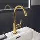 Waschtischarmatur in Brushed Gold von Ideal Standard. Sie hat einen hohen Auslauf und einen seitlichen Hebel zur Wassersteuerung, montiert auf einem weißen Waschbecken.